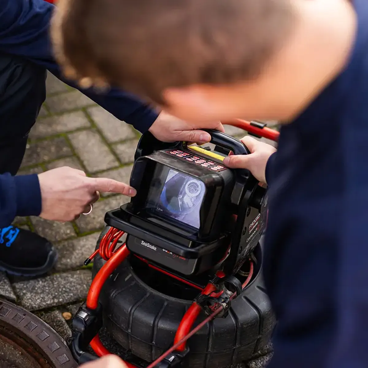 Zwei Techniker der MB Kanaltech München GmbH steuern die Kanalkamera am Schacht
