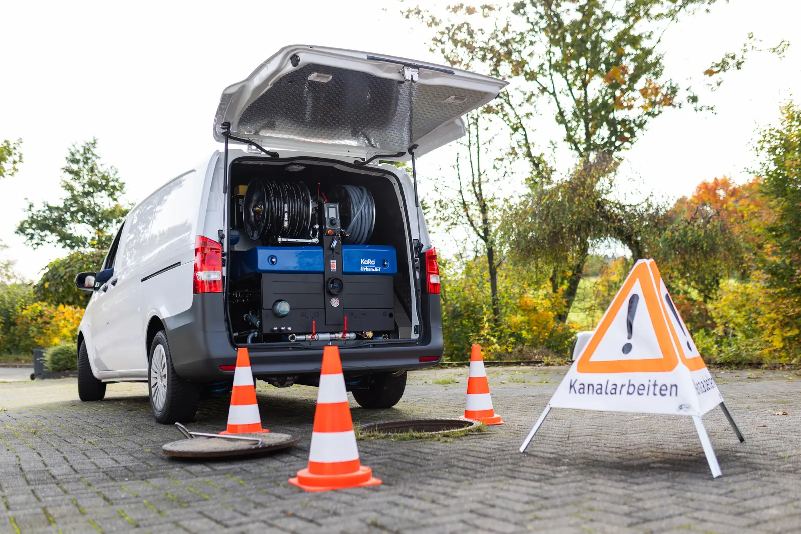 Einsatzfahrzeug mit Absperrung und Schild Kanalarbeiten am Schacht
